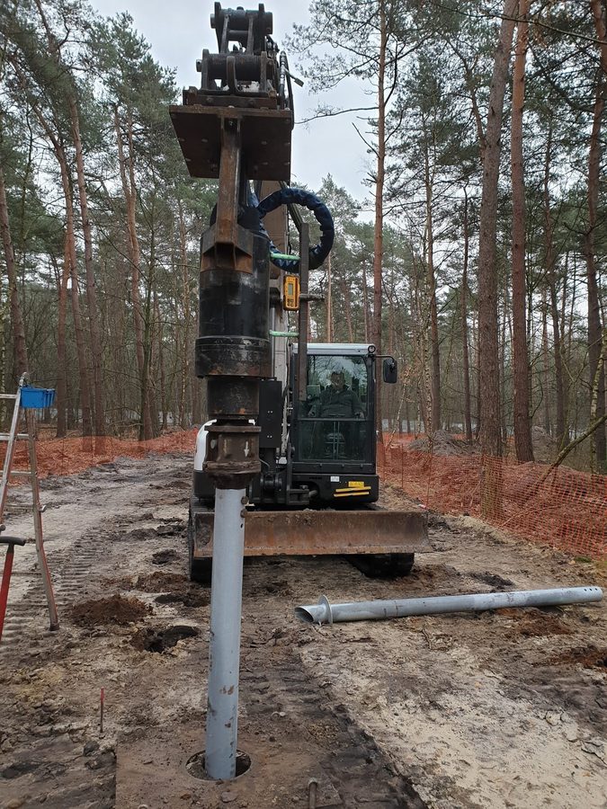 Bagger installiert verzinkten Schraubpfahl zwischen Kiefern im Wald von Bosland, Belgien